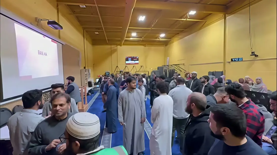 A hall full of brothers talking after a program, a slide on the screen behind them.